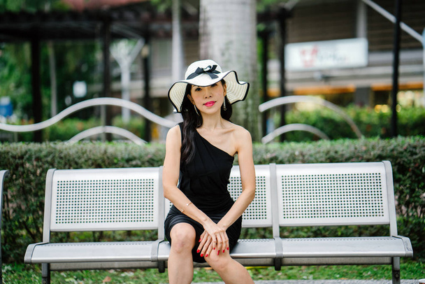 Portrait of Asian Chinese woman in an elegant  black dress posing on hat during the day in a park in Asia. - Foto, Imagen