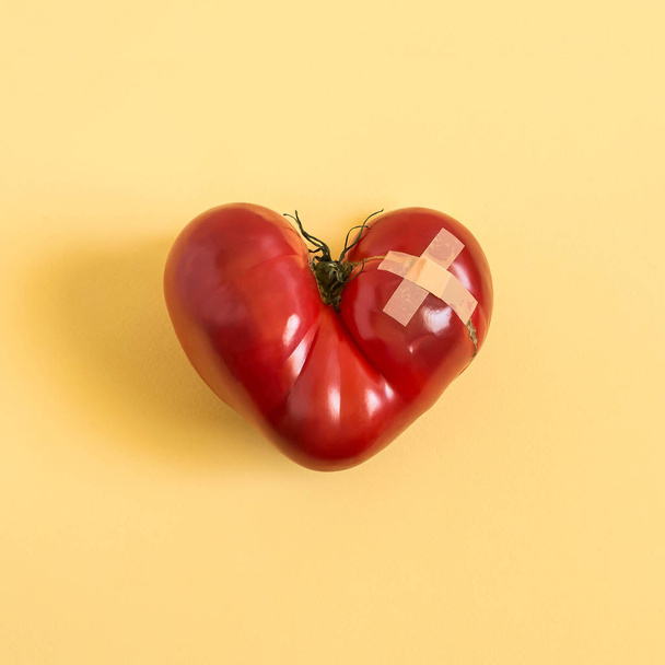 Yapıştırıcı ile yaralı kalp şeklinde büyük domates sarı zemin üzerine alçı. En az tarzı. Şakalar, Doğa, hayal ve fantezi. Kalp için yararlı besinler - Fotoğraf, Görsel