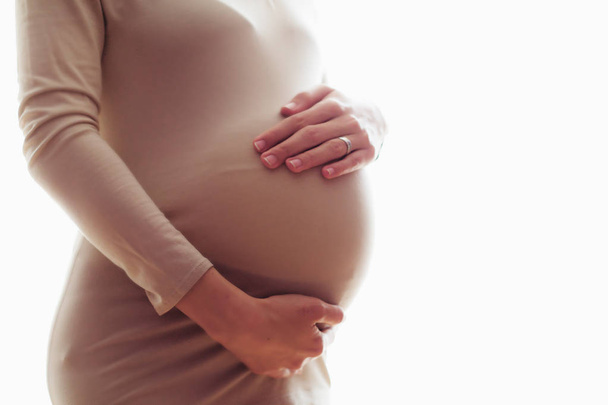 Vista laterale della donna incinta in abito beige che tiene la pancia isolata su sfondo bianco
 - Foto, immagini