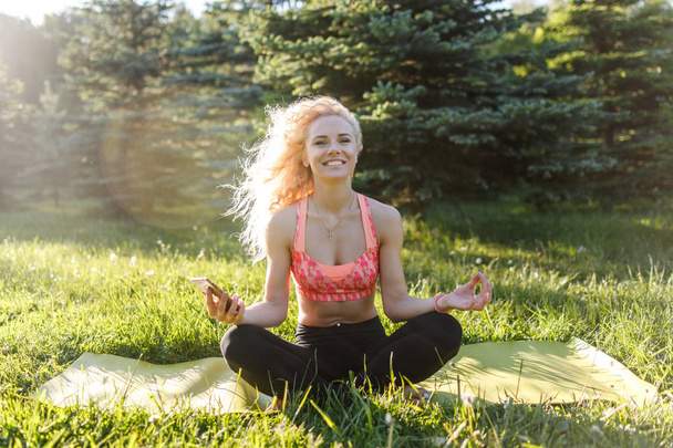 Image of young curly-haired sports woman practicing yoga on rug in park - Foto, imagen