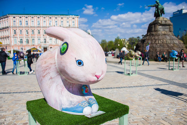 Easter Bunny shape in soft pink color with blue sneakers on his feet against the backdrop of monument to Bohdan Khmelnytskyi. Beautiful Easter decoration art - Fotó, kép