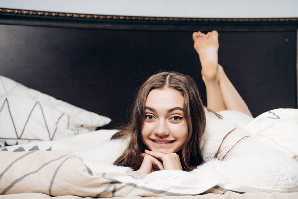 lovely beautiful girl lies in bed early in the morning, smiles and does not want to get up - Fotografie, Obrázek
