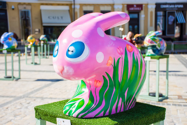 Sculpture of pink Easter Bunny amid ancient houses with painted flowers tulips on the side. Beautiful Easter art decoration. Kyiv (Kiev), Ukraine, april 2018. - Fotó, kép