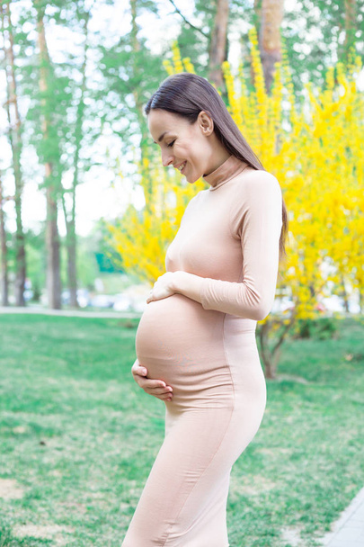 Partial view of pregnant woman smiling walking in park and holding belly - Fotoğraf, Görsel