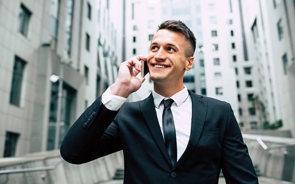 Portrait of happy young businessman talking using smartphone on city background - Foto, Imagen