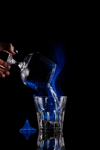 partial view of woman pouring burning sambuca alcohol drink into glass on black background - Fotoğraf, Görsel