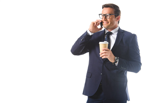 happy businessman in eyeglasses talking on smartphone and holding paper cup of coffee isolated on white background  - Foto, Imagem