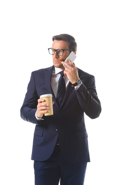 serious businessman in eyeglasses talking on smartphone and holding paper cup of coffee isolated on white background  - Φωτογραφία, εικόνα