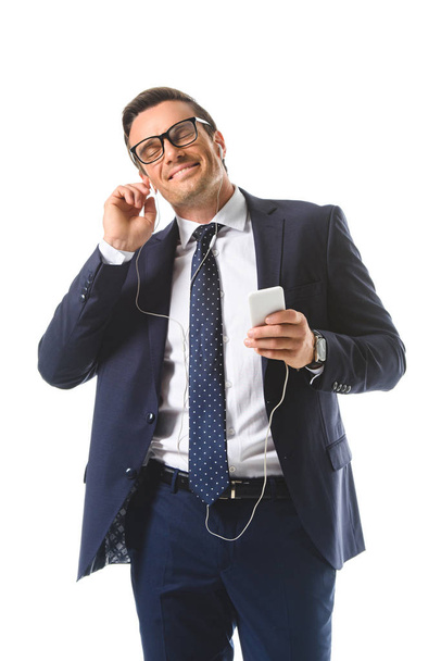 happy businessman in eyeglasses listening music in earphones with smartphone isolated on white background  - Zdjęcie, obraz