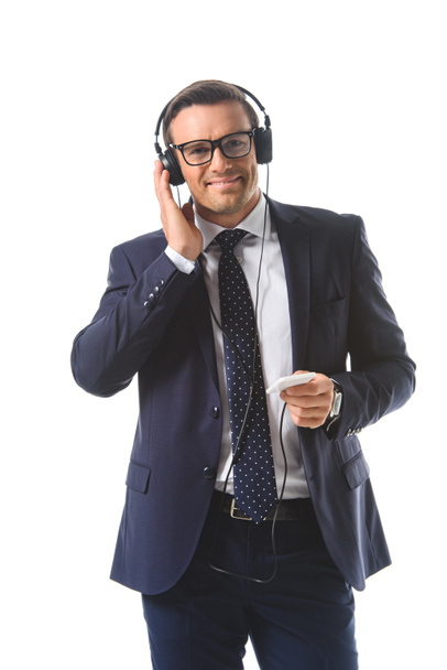 smiling businessman in eyeglasses listening music in headphones with smartphone isolated on white background  - Fotó, kép