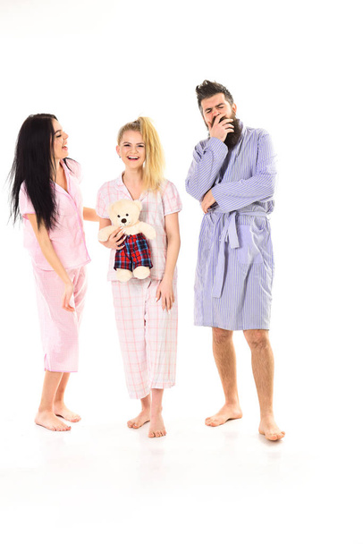 Man with beard and mustache, cute blonde and brunette girls with toy bear just wake up. Girls with bearded macho in pajamas and robe in morning, isolated white background. Sleepy morning concept - Photo, Image