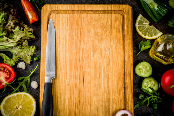 Cooking background, fresh salad ingredients, italian cuisine - tomatoes, olive oil, lemon, cucumbers, arugula, parsley, onions, with knife and cutting board, Dark rusty background copy space top view - Photo, image