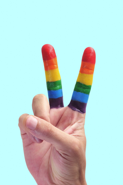 die Hand eines Mannes, der das V-Zeichen macht, mit den Fingern als Regenbogenfahne bemalt, vor blauem Hintergrund, mit etwas Leerstelle oben - Foto, Bild