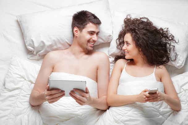 Overhead of beautiful young couple lying on the bed using tablet computer and smartphone - Foto, immagini