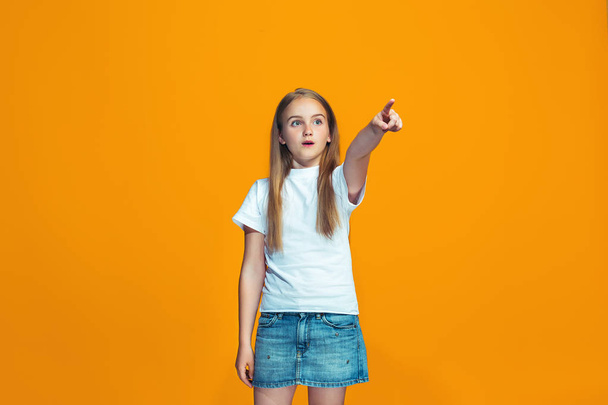 The happy teen girl pointing to you, half length closeup portrait on orange background. - Photo, Image