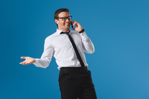 buisnessman feliz en gafas riendo mientras habla por teléfono inteligente aislado en azul
 - Foto, Imagen