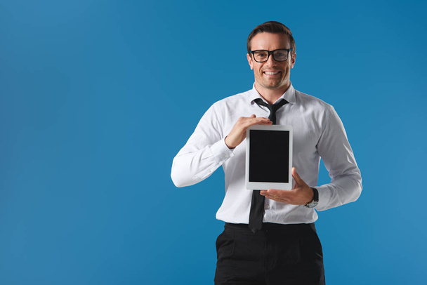 handsome man in eyeglasses holding digital tablet with blank screen and smiling at camera isolated on blue - Foto, Bild