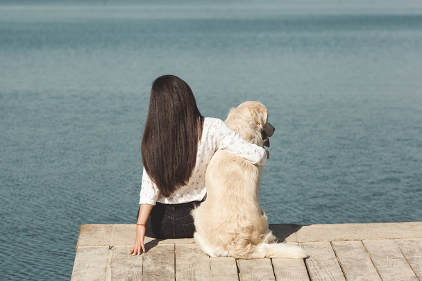 Young attractive woman sitting at the pier with her dog. Best friends outdoors - Fotografie, Obrázek