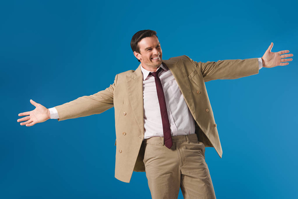 cheerful man standing with open arms and looking away isolated on blue - Photo, Image