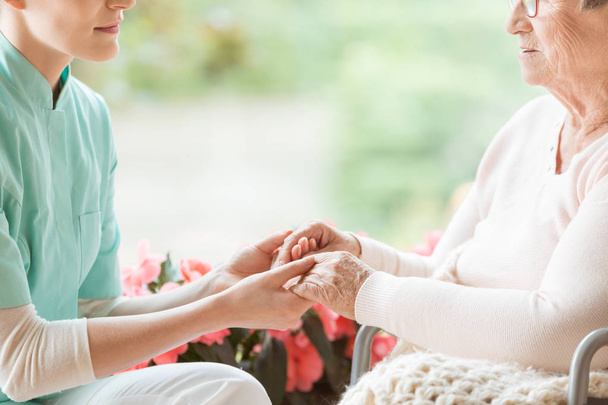 Nurse holding hands of disabled elderly woman in a wheelchair - Photo, Image