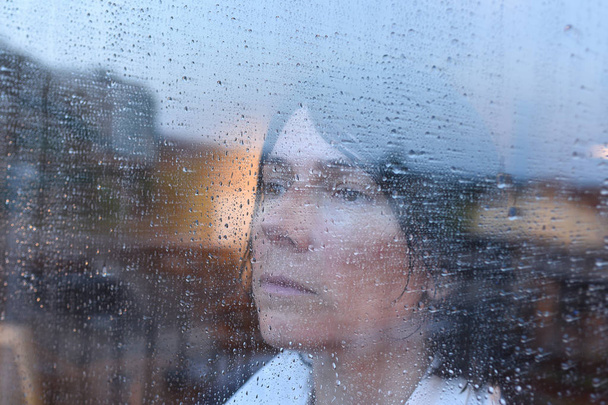 Mujer mirando por la ventana en un día lluvioso
 - Foto, imagen