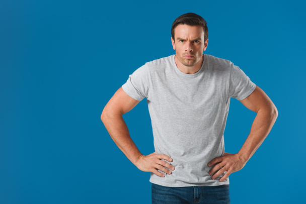 frowning man standing with hands on waist and looking at camera isolated on blue - Fotografie, Obrázek
