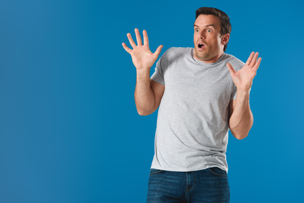 потрясенный мужчина поднимает руки и смотрит в сторону изолированных на синий
 - Фото, изображение