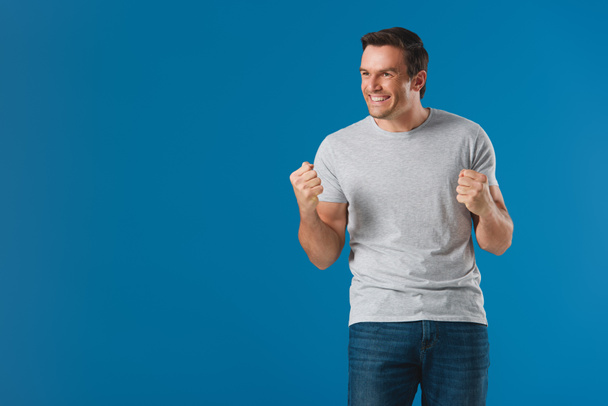 happy man shaking fists and looking away isolated on blue - Photo, Image