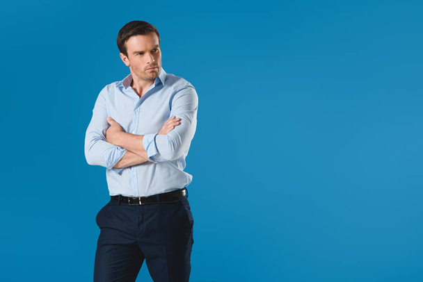 serious man standing with crossed arms and looking away isolated on blue - Photo, image