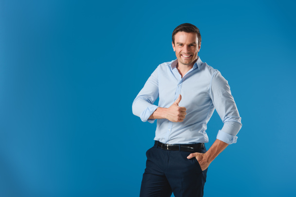 handsome businessman showing thumb up and smiling at camera isolated on blue - Фото, изображение