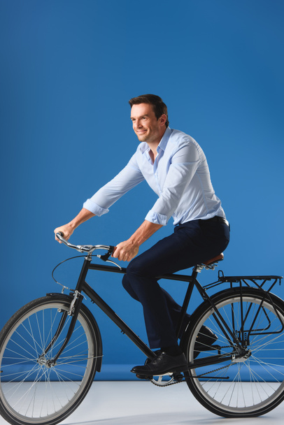 smiling businessman riding bicycle and looking away on blue - Fotografie, Obrázek