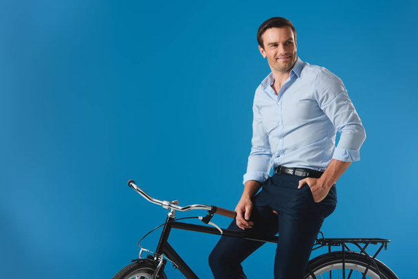 bel homme souriant assis sur le vélo et regardant loin isolé sur bleu
 - Photo, image