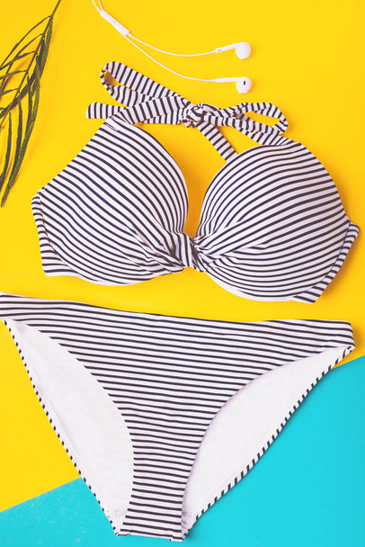 Top view of two pieces striped blue and white swimming suit on blue and yellow pastel background. Copy space. Concept of vacation. - Foto, immagini