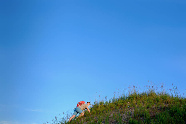 traveler with orange backpack hiking in the hills on blue sky background - Foto, imagen