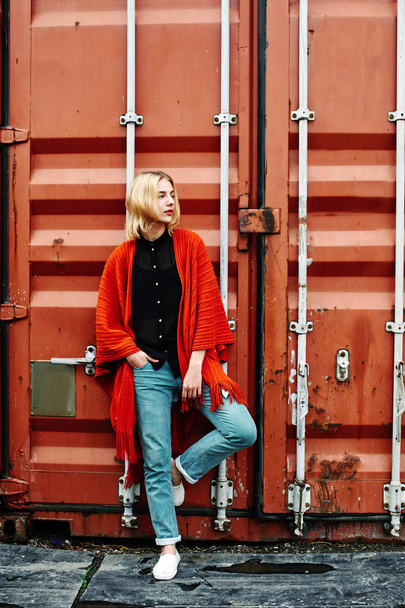 blonde woman wearing stylish clothes posing on background of red cargo container - Foto, immagini