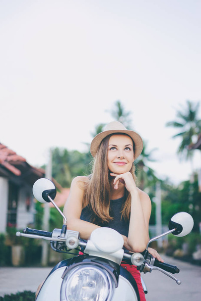 Outdoor portrait of pretty young woman in hat sitting on scooter. - 写真・画像