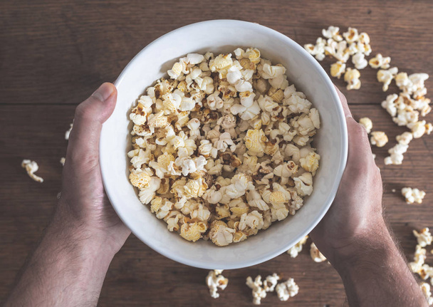 hands holding bowl filled with popcorn above wooden table - Photo, Image