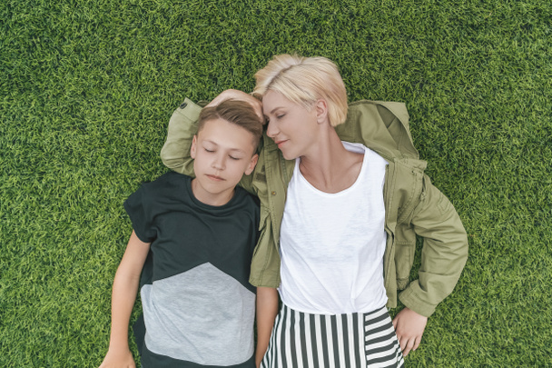 ylhäältä kaunis äiti ja poika suljetuin silmin makaa yhdessä vihreällä nurmikolla
 - Valokuva, kuva