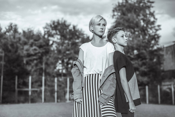 black and white photo of mother and son looking away while standing back to back in park - Photo, Image