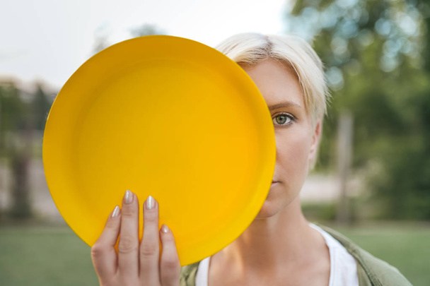 bela mulher loira segurando disco voador amarelo e olhando para a câmera
 - Foto, Imagem