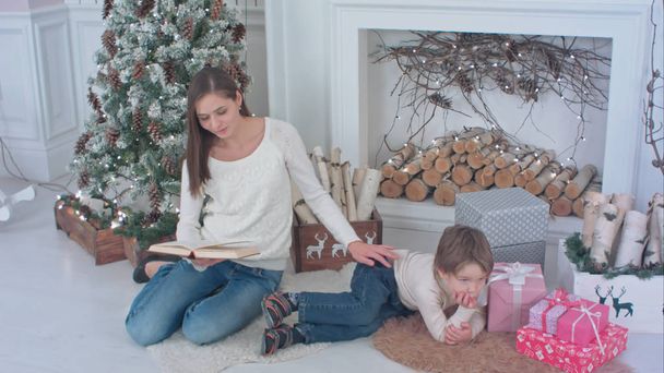 Mother reading a book for her little son lying near Christmas tree - Foto, imagen