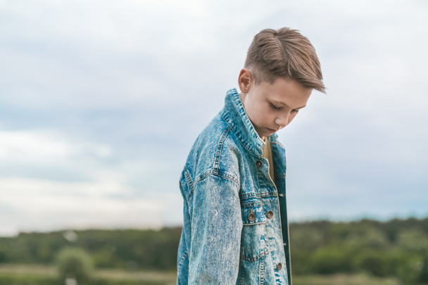 beautiful boy in denim jacket looking down at cloudy day - Photo, Image