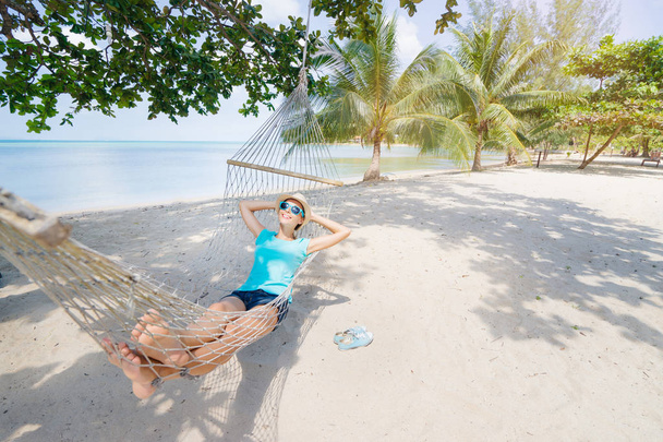 Young pretty woman in hat and sunglasses laying in hammock on the beach. - Fotoğraf, Görsel