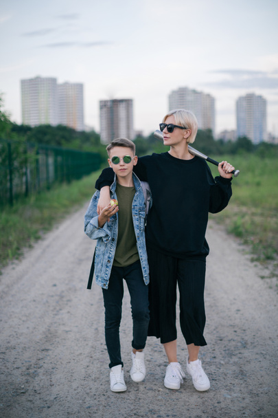 stylish mother and son in sunglasses standing with baseball bat on path - Foto, afbeelding