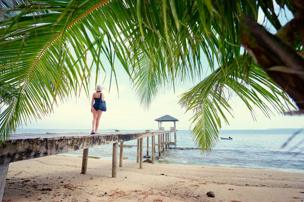 Young woman in swimwear and hat standing on the wooden beach pier. - Фото, изображение