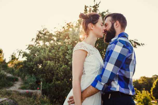 Beautiful guy and girl hugging and kissing. Love story photo on outdoor in sunset light. Couple in love. Pretty girl and brutal bearded guy in outdoor. - 写真・画像