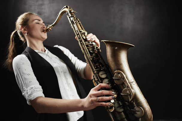 Young woman playing saxophone on black background - Foto, imagen