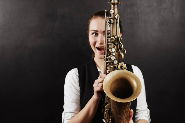woman holding saxophone on black background  - Фото, изображение