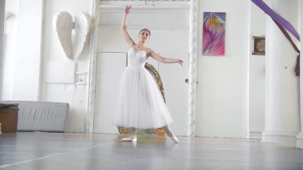 Jonge aantrekkelijke ballerina in een witte tutu poseren in ruime witte studio, slow-motion - Video