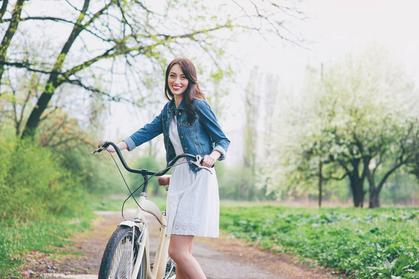 Attractive young brunette woman  walking with a bicycle against nature background. - Φωτογραφία, εικόνα